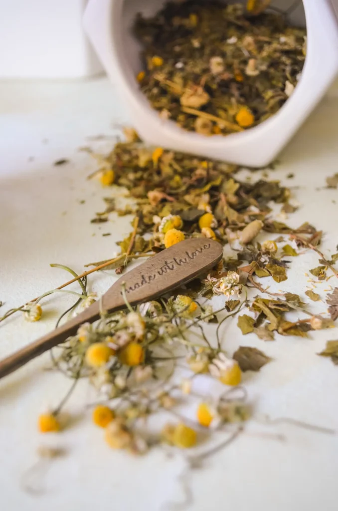 Chamomile flowers and a wooden spoon with loose dried chamomile, placed on a white surface.