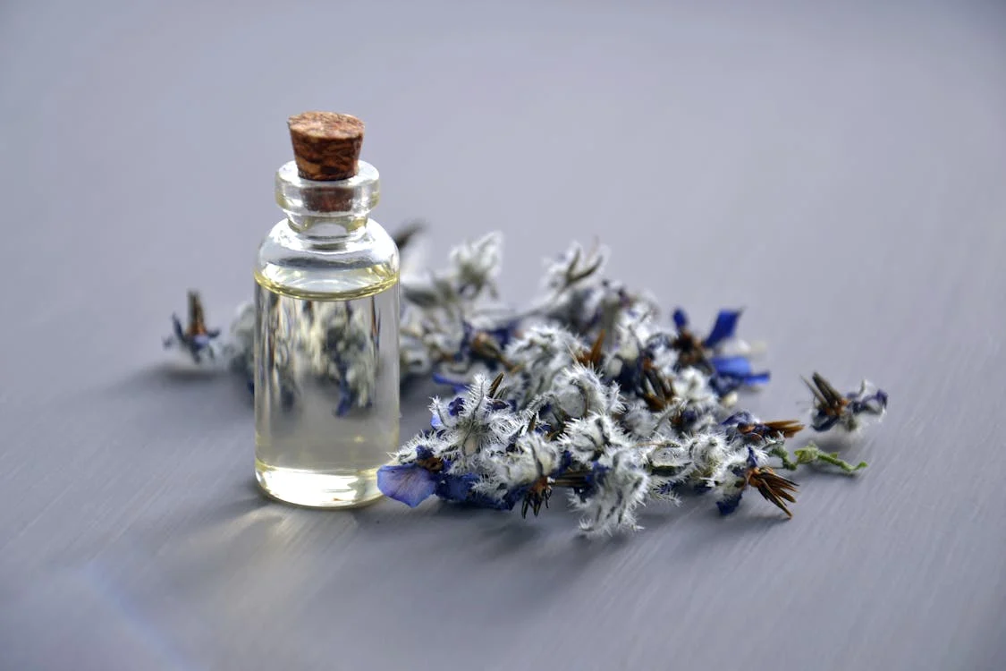 A small glass bottle of essential oil surrounded by delicate lavender flowers, symbolizing aromatherapy for better sleep and relaxation.