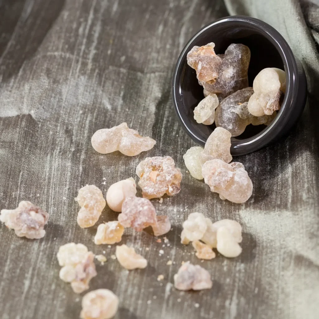 Bottle of frankincense essential oil with resin pieces spilling from a jar on a soft fabric background.